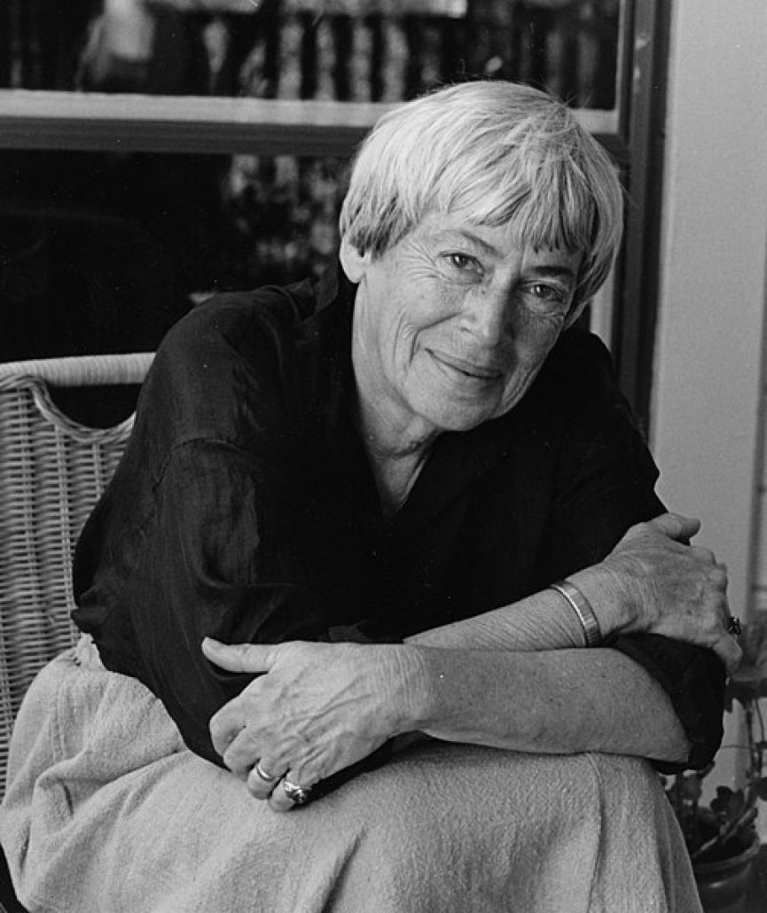 foto em preto e branco de Ursula K Le Guin sentada, com braços cruzados